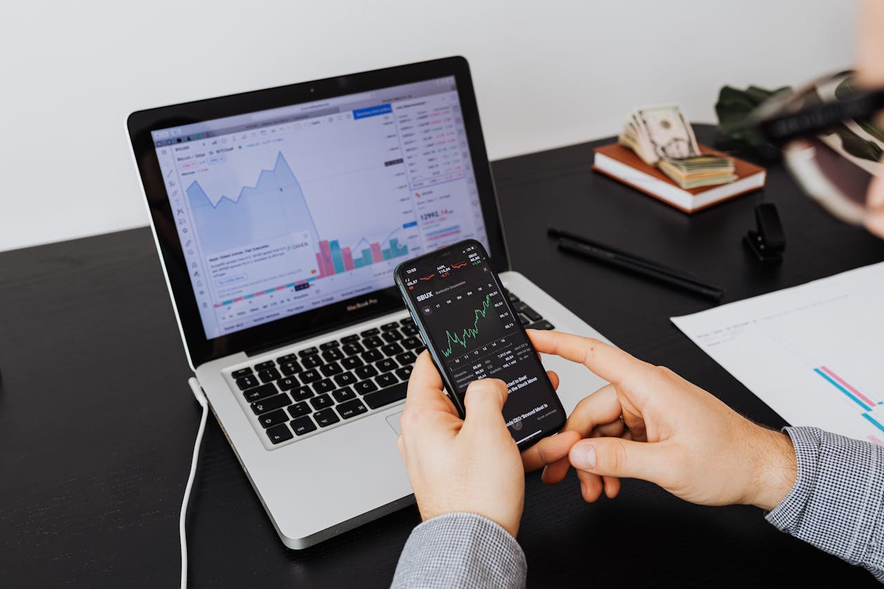 Services Person analyzing stock market data on a laptop and smartphone indoors.